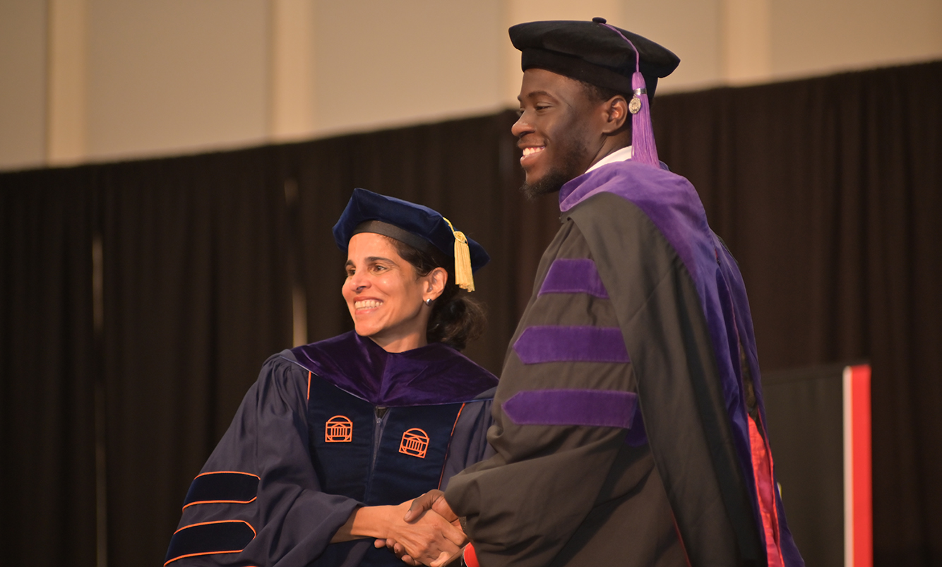 Dean Rodrigues shakes hands with Michael Modupe Faleye while handing the new graduate his diploma. Photo by Dennis McDaniel.